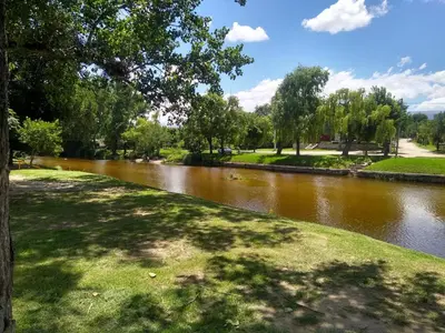 a river in a park with a tree and grass at Las Cuatro Estaciones in Villa Cura Brochero
