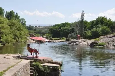 a bench with an umbrella next to a river at Departamento de alquiler temporario in Villa Carlos Paz