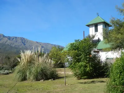 a white building with a green roof with mountains in the background at Finca La Julia in Luyaba