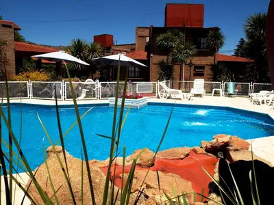 a large blue swimming pool with chairs and umbrellas at Cabañas La Aldea in Villa Carlos Paz