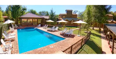 a swimming pool with chairs and umbrellas next to a house at Posada Pfullendorf - Adults Only in Villa General Belgrano