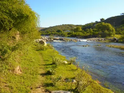 a river with green grass and trees next to the water at al otro lado del río in San Francisco del Monte de Oro