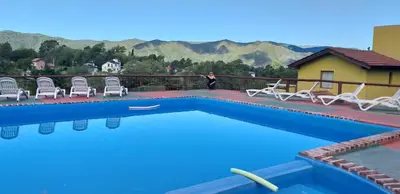 a pool with chairs and a man standing next to a house at Cabañas Wairoa Haus in Villa General Belgrano