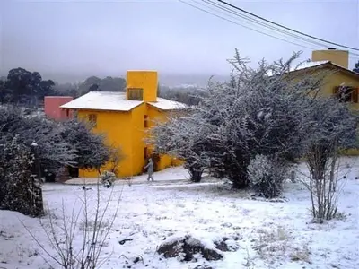 a yellow house with snow on the ground and trees at Cabañas Wairoa Haus in Villa General Belgrano