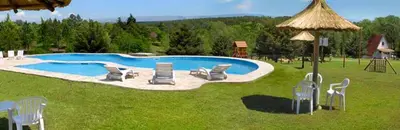 a swimming pool with chairs and an umbrella at Cabañas Juan Salvador in Los Reartes