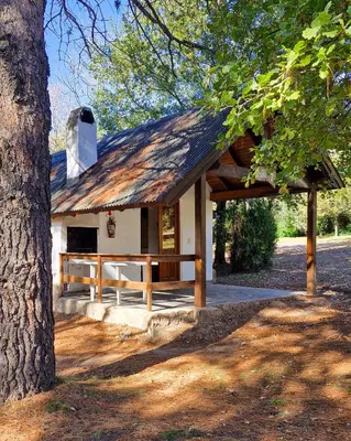 a small white house with a wood roof at Cabañas Am Bach in Villa General Belgrano