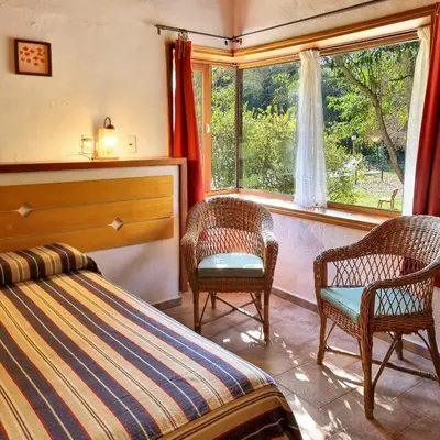 a bedroom with two chairs and a bed and a window at Cabañas Am Bach in Villa General Belgrano