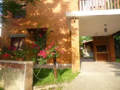 a house with a fence and a plant with pink flowers at Cabanas los lirios in Santa Rosa de Calamuchita