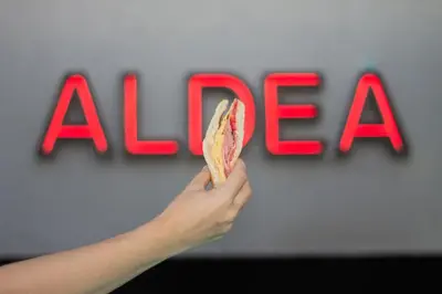 a person holding a piece of food in front of the alfa sign at Aldea Hostel & Café in Cordoba