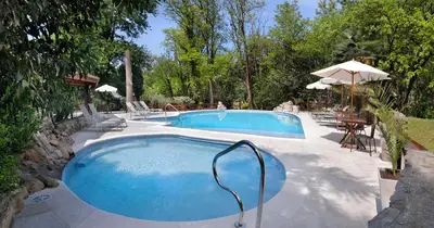 a swimming pool in a yard with tables and umbrellas at Posada del Sauce in Villa General Belgrano