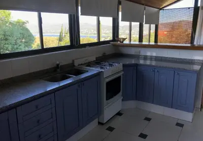 a kitchen with blue cabinets and a sink and windows at Hermosa casa con vista al lago in Villa Carlos Paz
