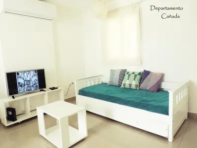 a white bedroom with a bed and a tv at Departamento Cañada Güemes