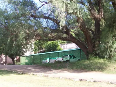 a green fence with cars parked in a parking lot at Costa Serrana Apart Hotel in Mina Clavero