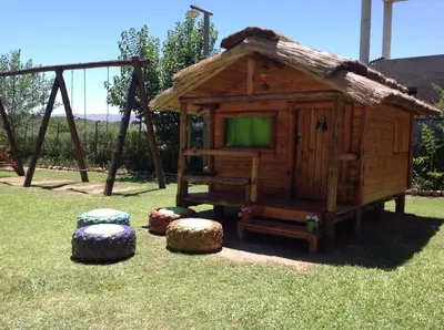 a small wooden cabin with stools in the grass at CABAÑAS VIEJO VIVERO in Mina Clavero