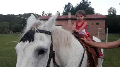 a little girl riding on the back of a white horse at Cabañas Landhaus in Villa General Belgrano