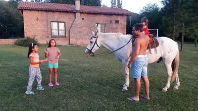 a man and two children standing next to a white horse at Cabañas Landhaus in Villa General Belgrano