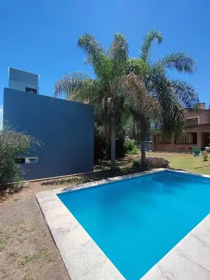a blue swimming pool in front of a house with palm trees at Casa en Barrio Costa Azul in Villa Carlos Paz