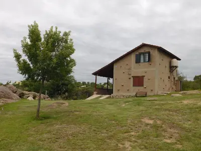 a building on a hill with a tree in a field at Cabañas las Vertientes in Villa Parque Siquiman