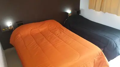 two beds in a bedroom with an orange blanket at Posada Entre Dos in Mina Clavero