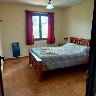 a bedroom with a bed and a window with red curtains at La Ponderosa Cumbrecita in La Cumbrecita