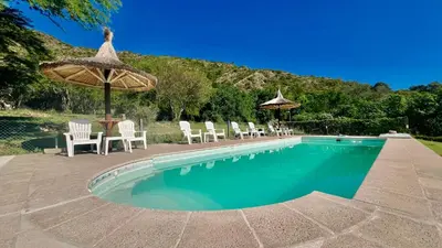 a swimming pool with chairs and an umbrella at Fincas del Faldeo in Villa General Belgrano