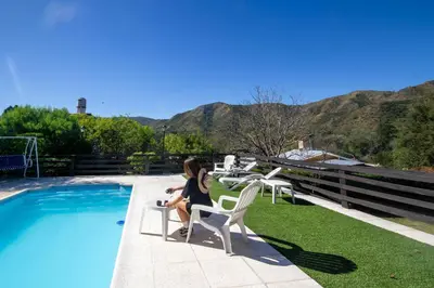 a woman sitting on a chair next to a swimming pool at Cabañas Noscohue in Villa General Belgrano
