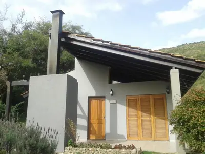 a small white house with a brown door at Cabañas Loma Azul in Villa General Belgrano
