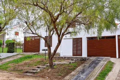 a tree in front of a white house at CASA FRENTE AL RIO Playas de Oro in Villa Carlos Paz