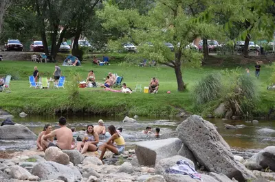 a group of people sitting on rocks in a river at CASA FRENTE AL RIO Playas de Oro in Villa Carlos Paz