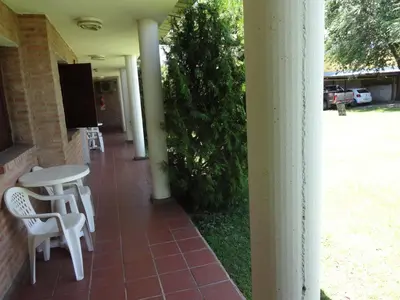 a porch with white chairs and a table and a bush at Rincón del Valle in Mina Clavero