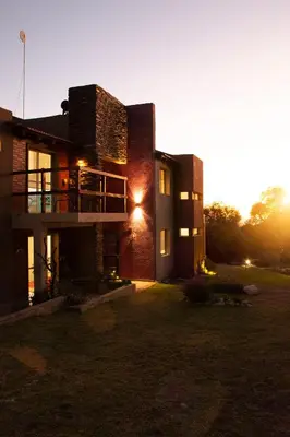 a house with the sun setting behind it at COSTA COM Departamentos de Montaña in Merlo