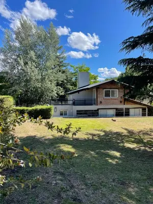 a house on a lawn with trees in the foreground at La Franca Cabaña de Veraneo in Villa General Belgrano