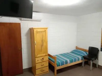 a room with a bed and a cabinet and a chair at Hostería El Peregrino in Villa Cura Brochero