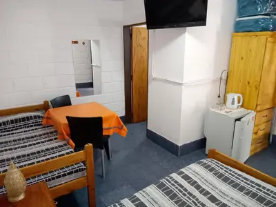a room with a table and two beds and a refrigerator at Hostería El Peregrino in Villa Cura Brochero