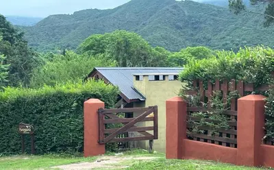a fence in front of a house with mountains in the background at Cabañas Kangarú in Santa Rosa de Calamuchita