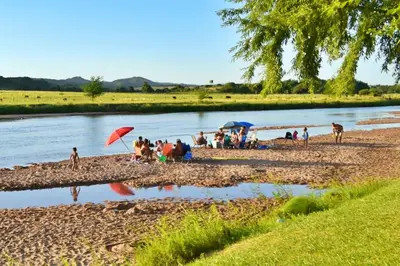a group of people sitting on a beach next to a river at BoraBora in Nono