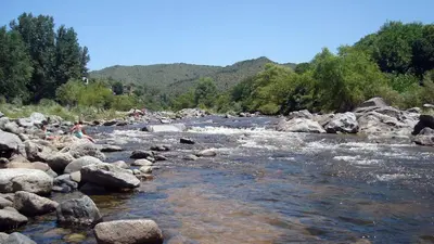 a river with rocks and people sitting on it at Soles Blancos Serranita in Alta Gracia