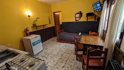 a small room with a bed and a table and a kitchen at Benvinguts Casa y Apartamentos de 1 a 12 personas Pleno Centro Santa Rosa de Calamuchita in Santa Rosa de Calamuchita