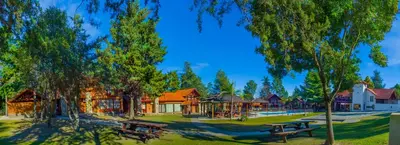 two picnic tables in a park with trees and buildings at Hotel Villa Sol in Merlo