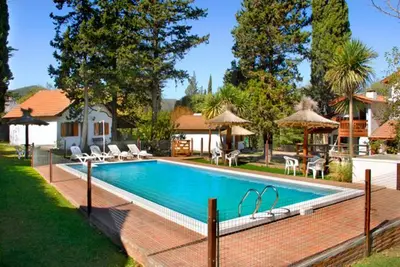 a swimming pool with chairs and umbrellas next to a house at Cabañas Los Duendes in Villa General Belgrano