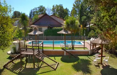 a backyard with a pool and a playground with chairs and a swing at Cabañas Los Duendes in Villa General Belgrano
