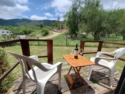 a table with a bottle of wine and two chairs at Cabañas Rosaditas in Santa Rosa de Calamuchita
