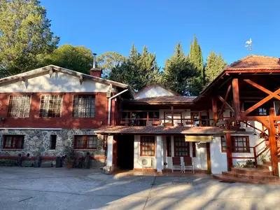a large wooden house with trees in the background at Hotel Samay Huasi in Villa General Belgrano