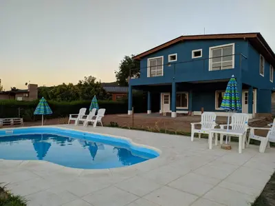 a blue house with white chairs and a pool at Complejo Cielo Azul in Villa Rumipal