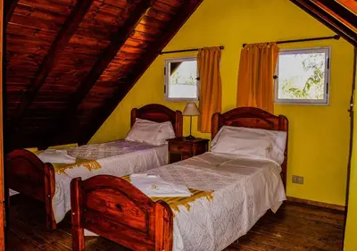 a bedroom with two beds and two windows at Cabañas Brisas del Cerro in Los Reartes