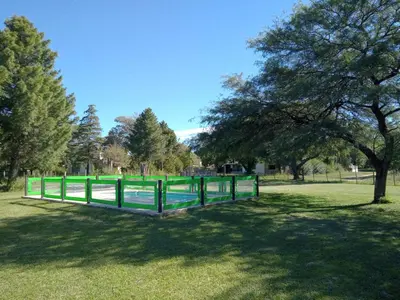 a green fence in a park with a tree at Cabaña Azul in Villa Anizacate