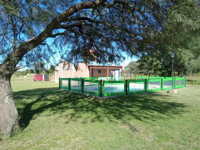 a green fence under a tree in a field at Cabaña Azul in Villa Anizacate