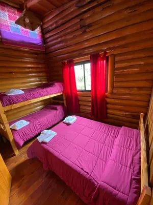 two beds in a log cabin with red curtains at Cabañas Los Álamos in Villa Carlos Paz