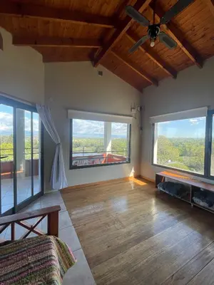 a living room with a ceiling fan and large windows at Casas Pura Vida in Villa General Belgrano