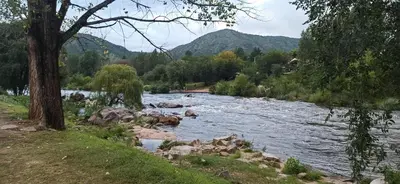 a river with rocks and trees and mountains in the background at Cabaña El Canal in Villa Carlos Paz